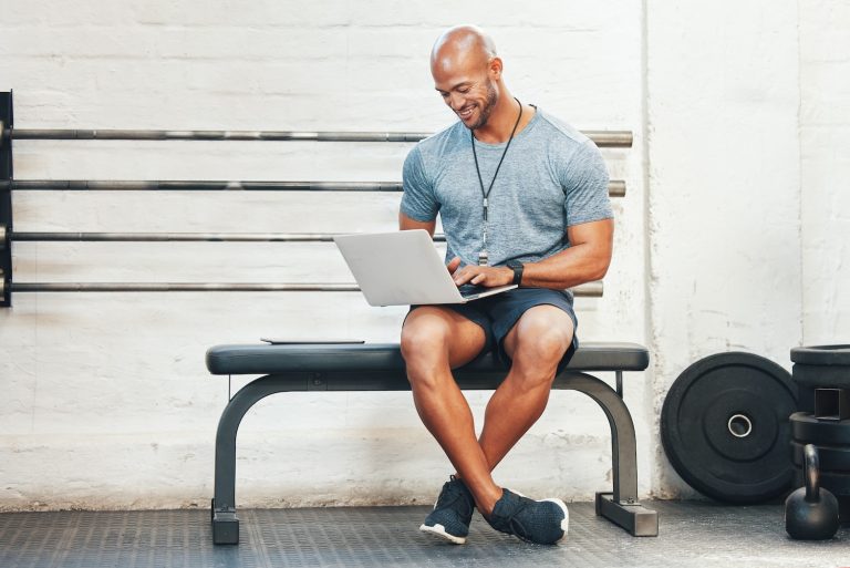 A man sitting on a bench looking down at a laptop on his lap