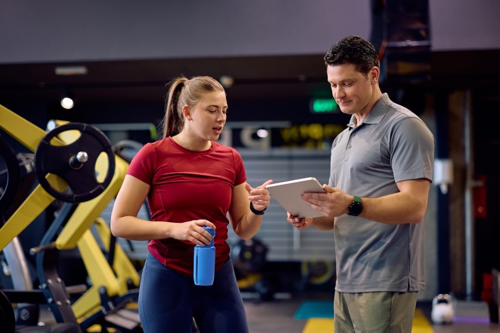 A personal trainer showing a client their digital tablet inside a gym
