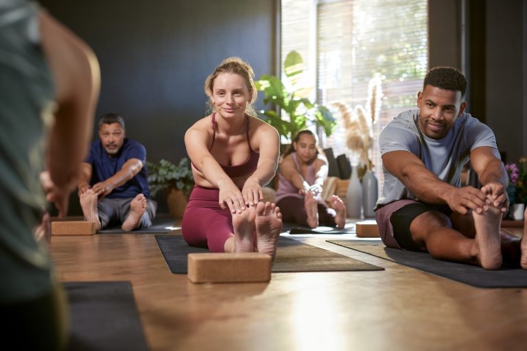 A group of men and women stretching to touch their toes during a yoga class indoors