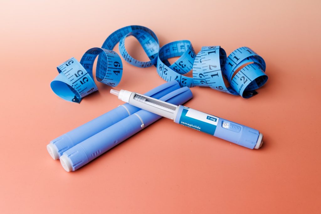 A blue and white syringe next to a blue measuring table on a peach background