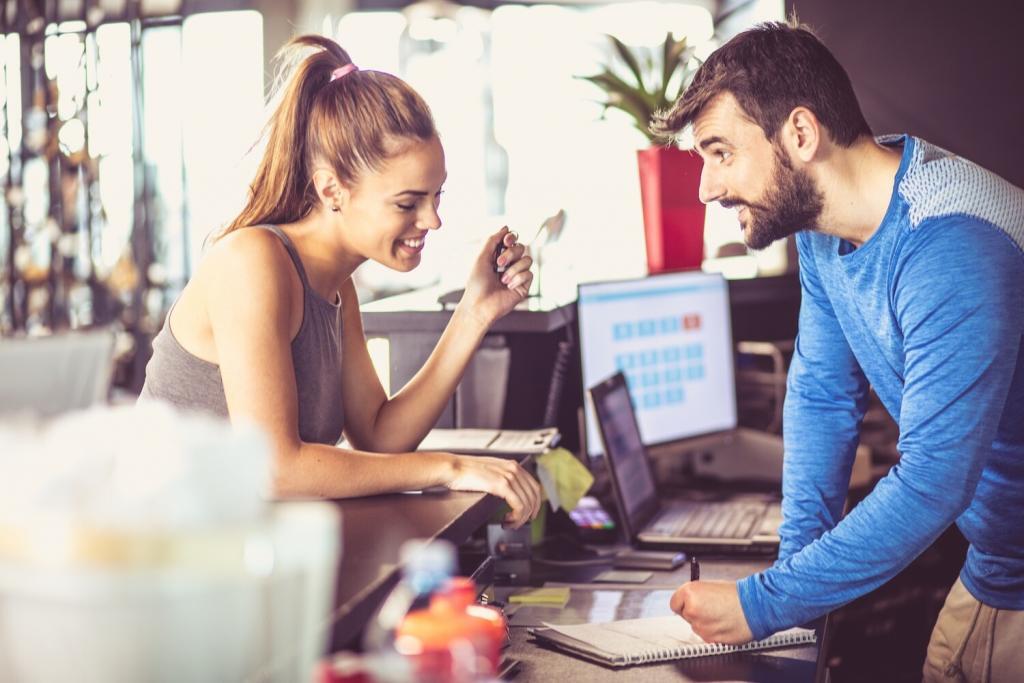An athletic woman talking to an athletic man at the front counter of a gym