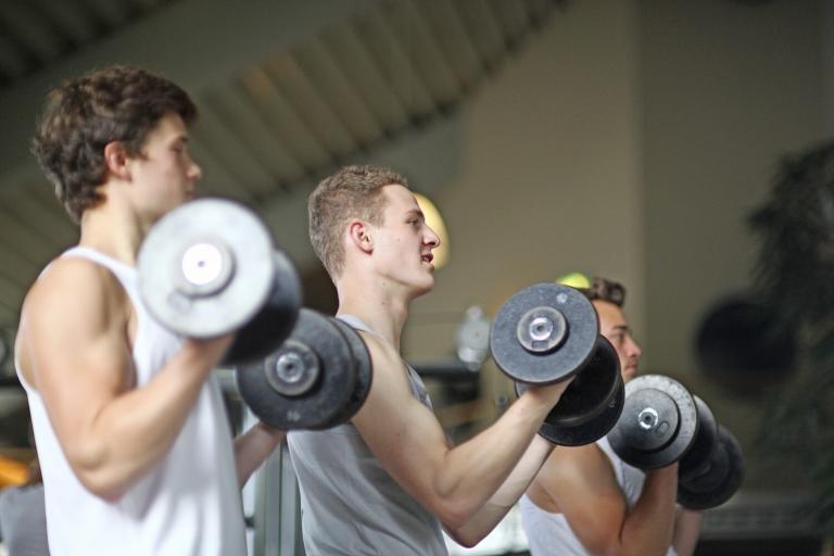 Three teenage boys training with dumb bells in a gym