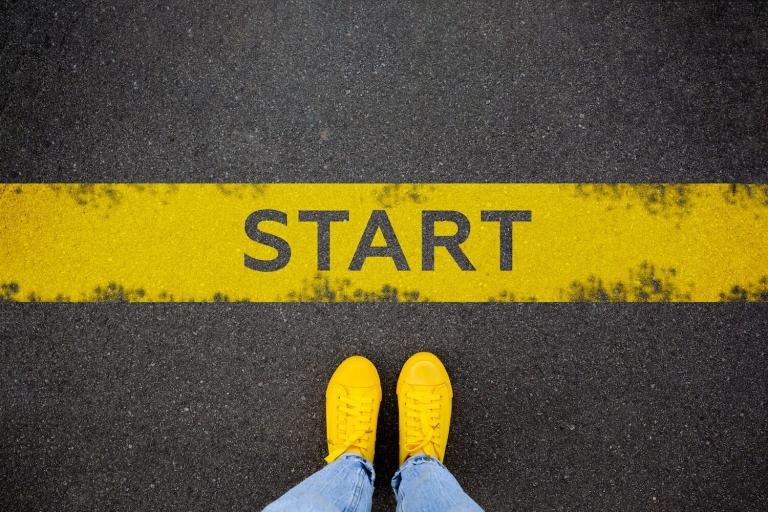 Female feet in yellow sneakers standing on street background with word new start written. Yellow race line beginning idea concept. Top view. Businessman of starting